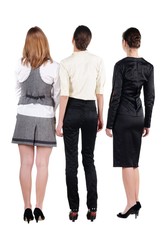 three beautiful young bussineswoman looking at wall. Rear view.