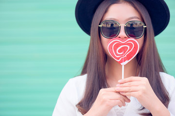Young woman's Valentines day.Asian Chinese young woman having fun with red lollipop over cyan background.