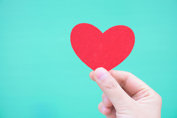 Valentines day and love concept.The hand holding a red heart shape decorations on cyan background.