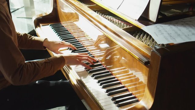 Playing piano. The young man plays a piano. The beautiful pianist plays melodies. Pleasant light from a window indoors. The Pproffesionalny pianist for a piano. Hands it is close to the camera. The
