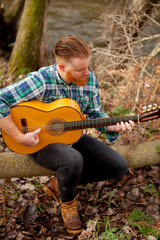 Hipster man with red beard with a guitar in the field