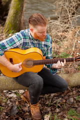 Hipster man with red beard with a guitar in the field