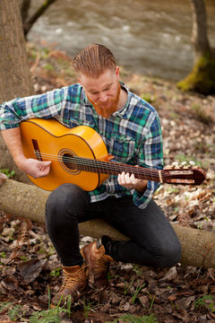 Hipster man with red beard with a guitar in the field