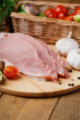 Slices of raw pork meat and wicker basket with vegetables