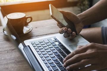 Hands holding mobile phone and working on computer typing laptop keyboard using wifi cyber internet online for business communication