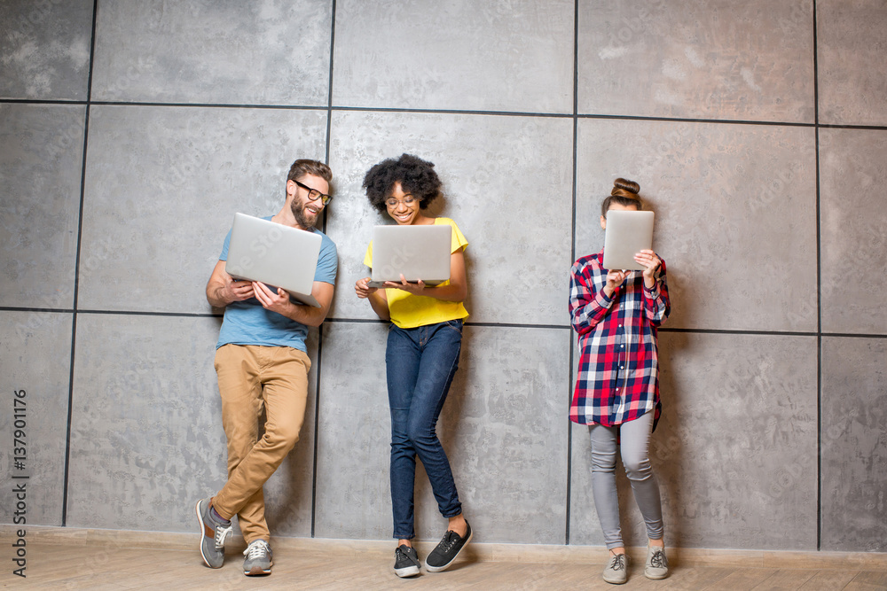 Wall mural Multi ethnic coworkers dressed casually in colorful clothes working with different gadgets on the gray wall background