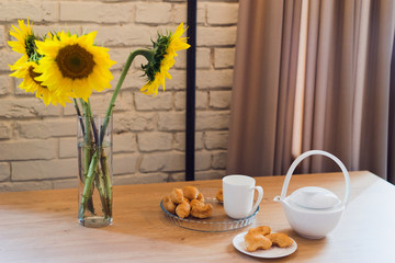 Coziness at home. Modern interior design. Bouquet of sunflowers on the dining table. Breakfast or snack with tea and croissants.