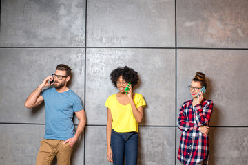 Fototapeta premium Multi ethnic coworkers dressed casually in colorful clothes talking with smart phones on the gray wall background