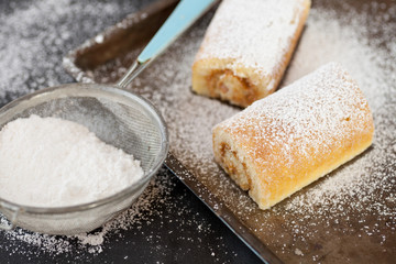 Fototapeta na wymiar Swiss rolls on baking tray with sieve and icing sugar