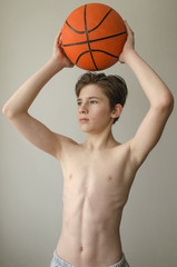 Teenager boy without a shirt with a ball for basketball on a light background
