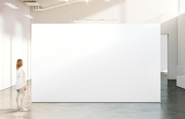 Woman walking near blank white wall mockup in modern gallery. Girl admires a clear big stand mock...