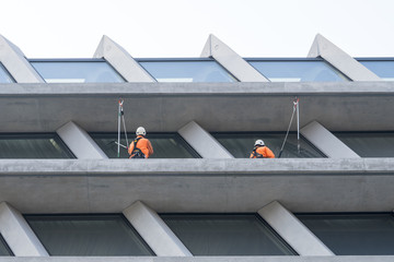 Window washers cleaning the glass facade of a modern building, high risk work.