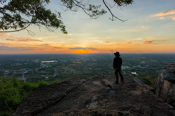 Young man traveler on cliff with beautiful landscape sunset over cliff and city