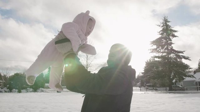 Dad Throwing Up and Catching Baby Girl Kissing Daughter Outside Playing in Front Yard with Winter Snow