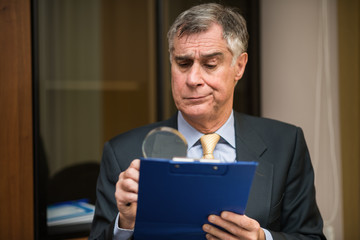 Businessman using a magnifying glass to read a document