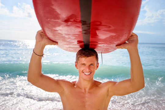 Portrait of surfer. Young man carrying surfboard on the sea beach.