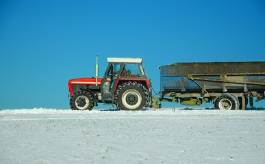 Tractor with trailer driving on snowy road.