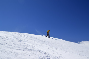 Snowboarder downhill on off-piste slope and blue clear sky