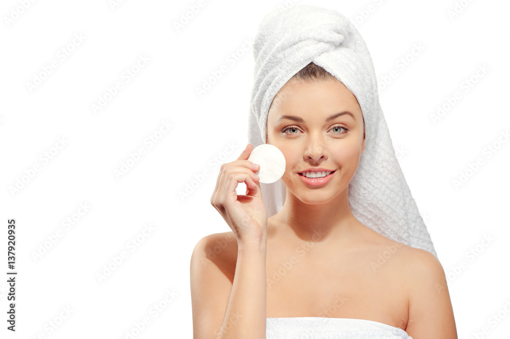 Wall mural young woman with a towel on her head removes makeup from the face with cotton pad