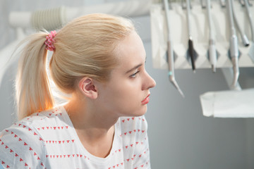 blonde girl sits on a background of dental instruments