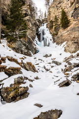 Fototapeta na wymiar Saent waterfall, in Val di Rabbi, Trentino Alto Adige, covered by snow in a day with clear sky with few clouds. Trees are without snow. It a typical winter / spring mountain landscape/scenery