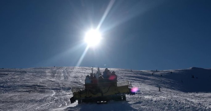 Skiers Riding on the Back of a Snowcat on a Snow Covered Mountain at a Winter Sunny Day