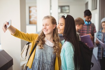  Smiling schoolgirls taking selfie with mobile phone in corridor