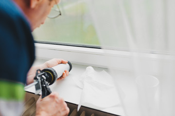 Backview of old man using a silicone tube  for repairing the window