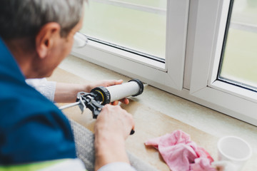 Backview of old man using a silicone tube  for repairing the window