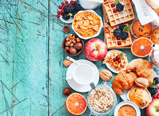 Healthy and colorful breakfast - cup of coffee with homemade granola, waffles, muffins,almond,hazelnuts,various fresh fruits, berries and milk on old wooden table.