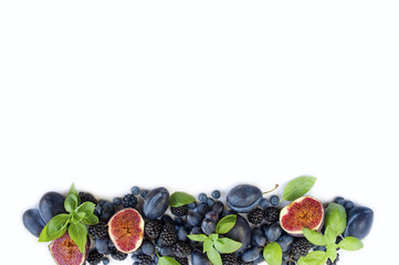 Blue and purple food. Group of fresh fruits and berries with basil's on a white background. Ripe blueberries, blackberries, grapes, plums and figs. Top view with copy space.