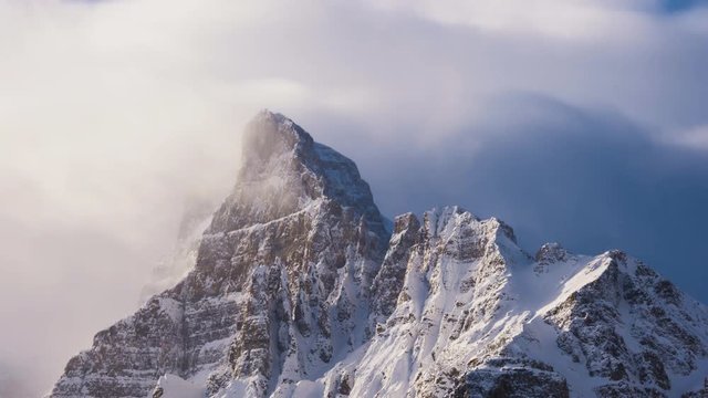 Time lapse clouds flowing over snowy mountain peak at sunrise