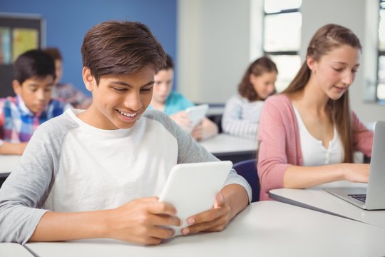 Students using digital tablet and laptop in classroom