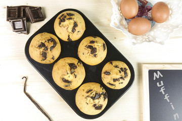 Muffin with chocolate drops in a muffin pan on wood background - top view