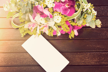 bouquet of flowers and white card on wooden table with warm lighting