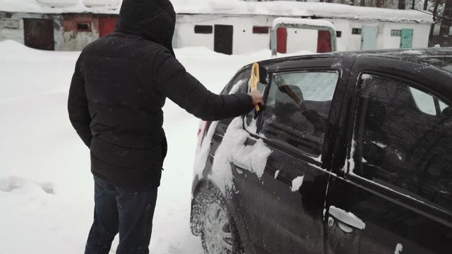 Transportation, winter, weather, people and vehicle concept - man cleaning snow from car with brush in living house district.