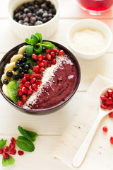 Healthy breakfast: fresh smoothie with kiwi, banana, garnet seeds, blueberry and coconut decorated mint leaves on white wooden table. Selective focus