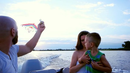 family launches kite sitting in a boat, the parents play with a child, ride on the speed of the boat, a happy child laughing, mother, father and son spend time in nature - Powered by Adobe