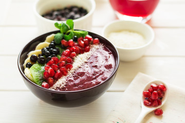 Healthy breakfast: fresh smoothie with kiwi, banana, garnet seeds, blueberry and coconut decorated mint leaves on white wooden table. Selective focus