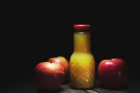 Apple cider vinegar in a glass jug, fresh apples, dark wooden background in rustic style, low key, selective focus