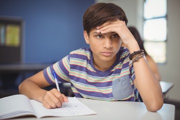 Tensed school boy doing homework in classroom