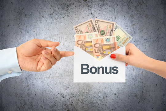 Woman Hand Giving A Bonus Or Additional Money On Envelope With Concrete Background