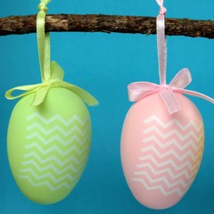 two decorative easter eggs hanging from a branch, with turquoise background