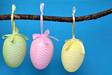 three decorative easter eggs hanging from a branch, with blue background