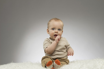 Cute baby boy sitting on the white blanket on the grey background