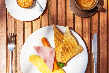 Morning Breakfast, food on wood table in cafe: Omlletee, ham, saussages, toast, cup of coffee and dessert. Top View