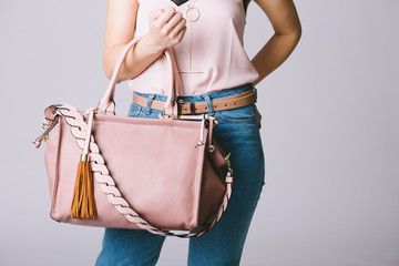 Fashionable young woman in casual clothes holding pink clutch isolated on gray background
