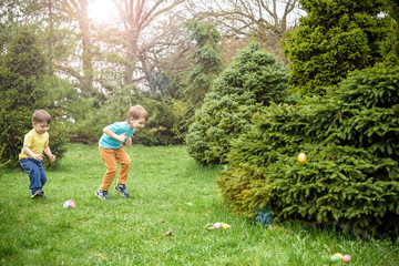 Kids on Easter egg hunt in blooming spring garden. Children searching for colorful eggs in flower meadow. Toddler boy and his brother friend kid  play outdoors