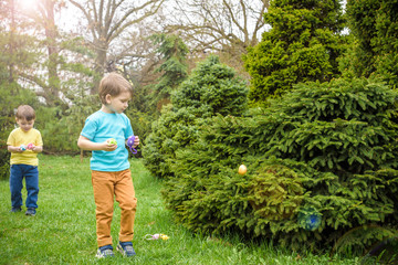 Kids on Easter egg hunt in blooming spring garden. Children searching for colorful eggs in flower meadow. Toddler boy and his brother friend kid  play outdoors