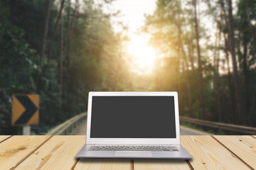 Laptop with blank screen on wooden table with dark misty forest